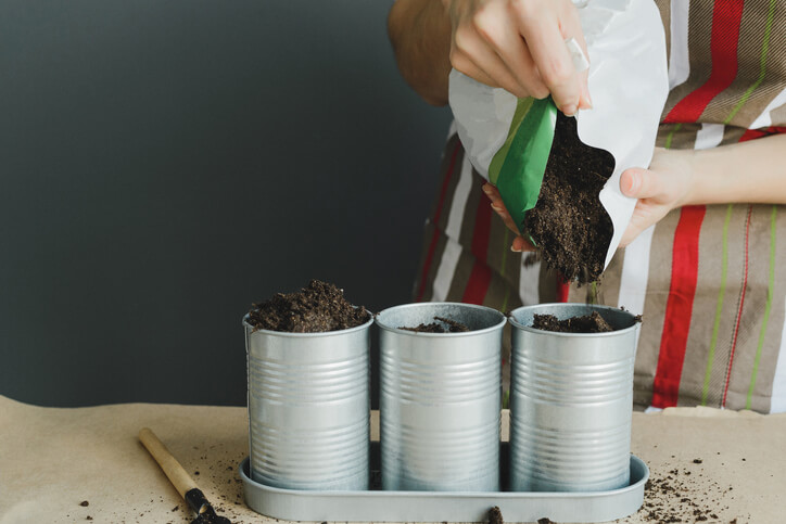 Person pouring potting soil into cans