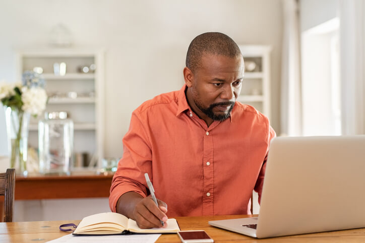 Man consulting a laptop while taking notes