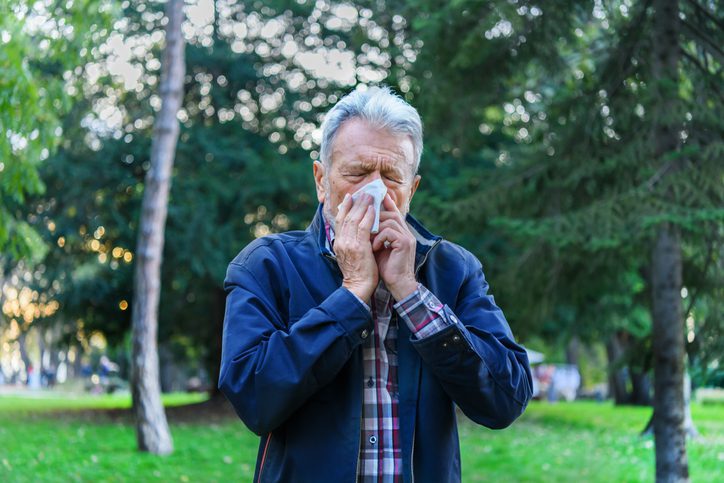 Man stands beneath trees, sneezing