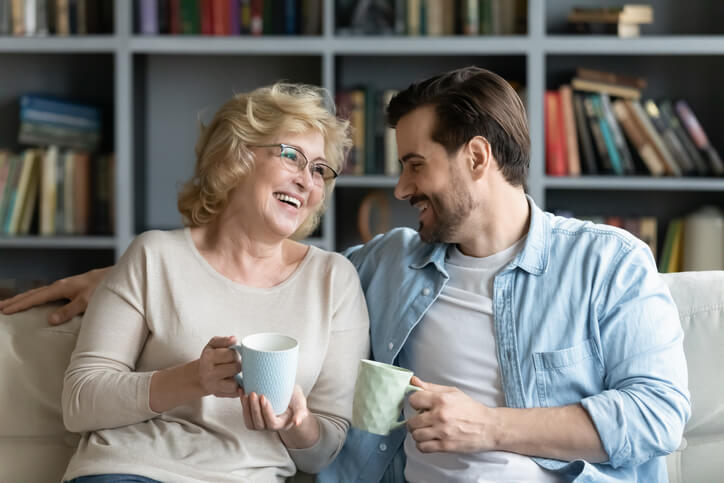 mother and adult son drink coffee on couch