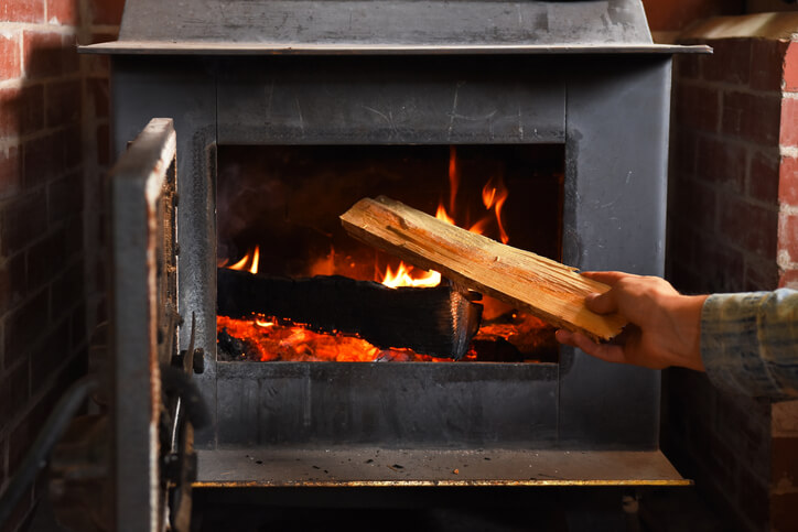 A person throwing logs into a woodburning stove