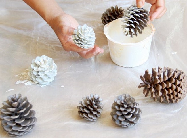 Person dipping pine cones in white paint