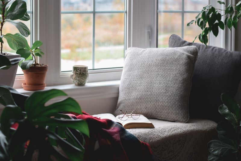 A woven throw pillow sits near plants and a coffee mug