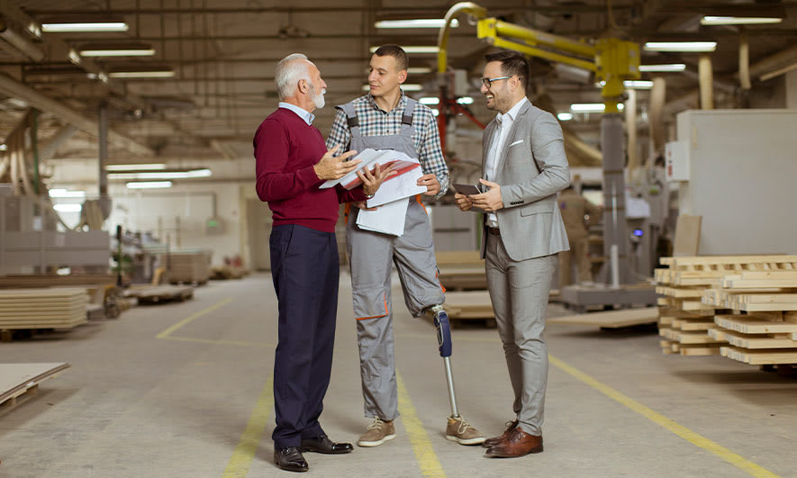 Three coworkers talk in a warehouse, one of them has a prosthetic leg