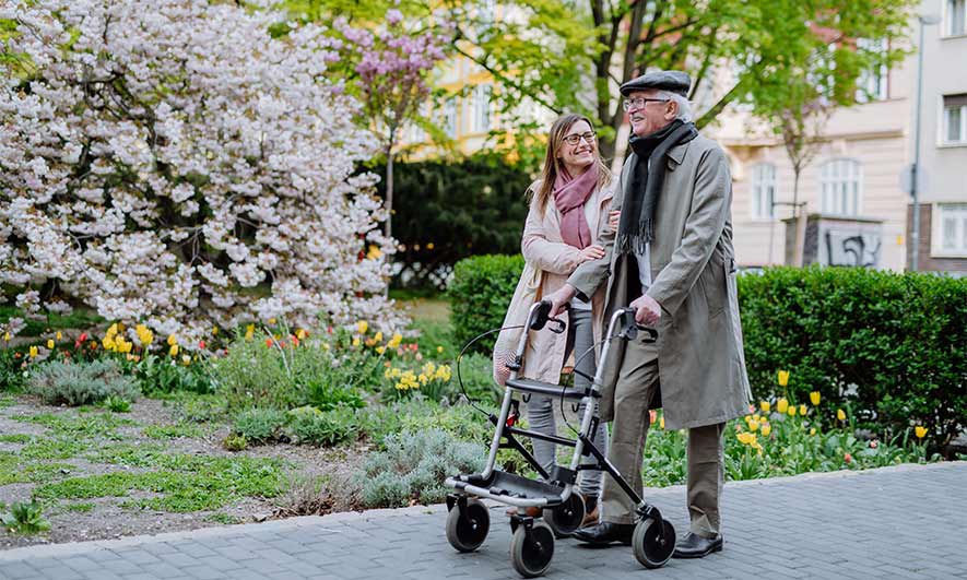 Two people walk in a park, one uses a walker