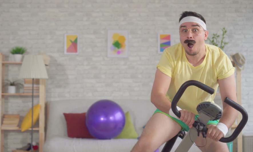 Man in a fake mustache falling off an exercise bike