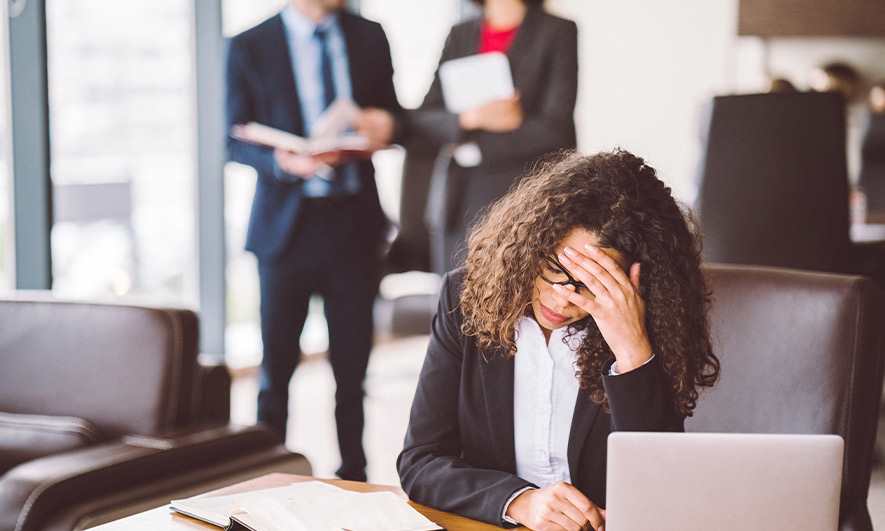 Business woman crying at desk while others laugh at her