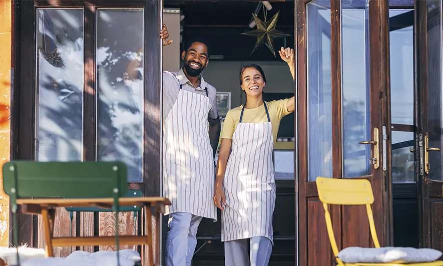 Two small business owners smile at their store entrance