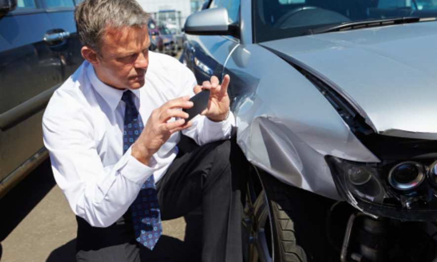 Man takes a picture of the damage on a car after a crash