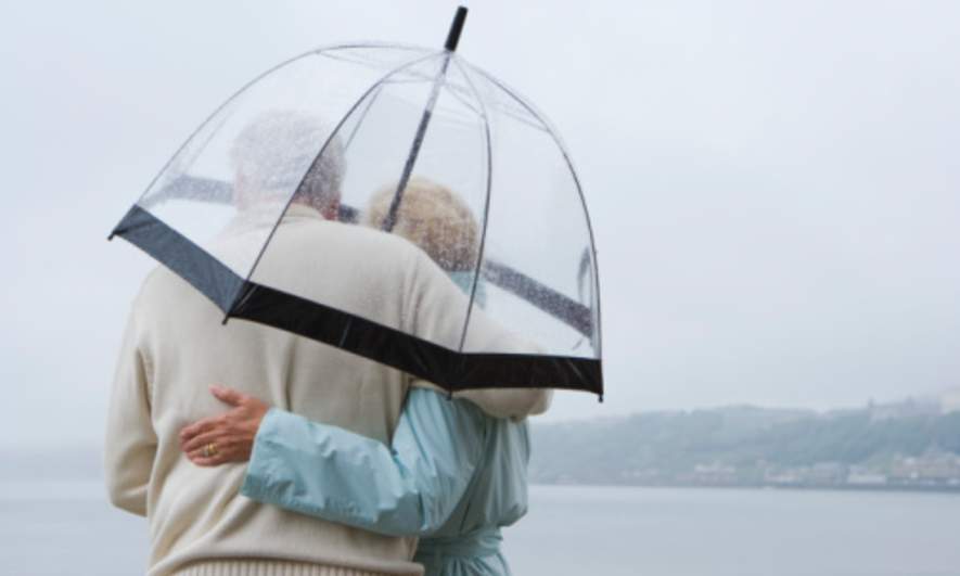 A middle-aged couple stands under an umbrella