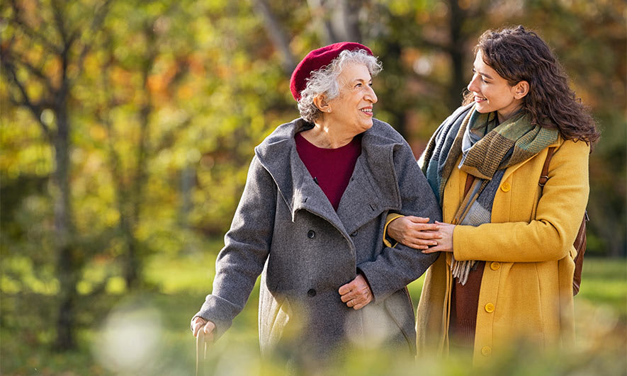 Caregiver walking with senior lady in park during autumn.