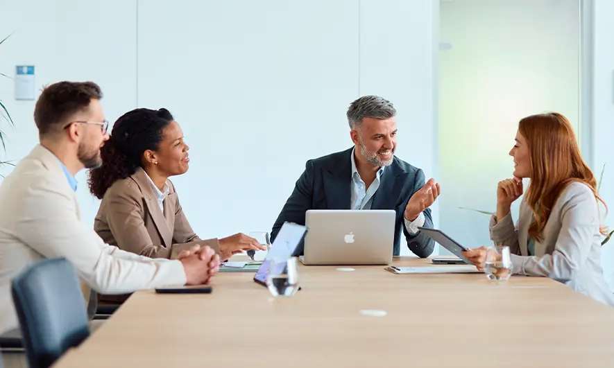 Business professionals seated around a conference table, engaged in a collaborative meeting with a laptop and documents.