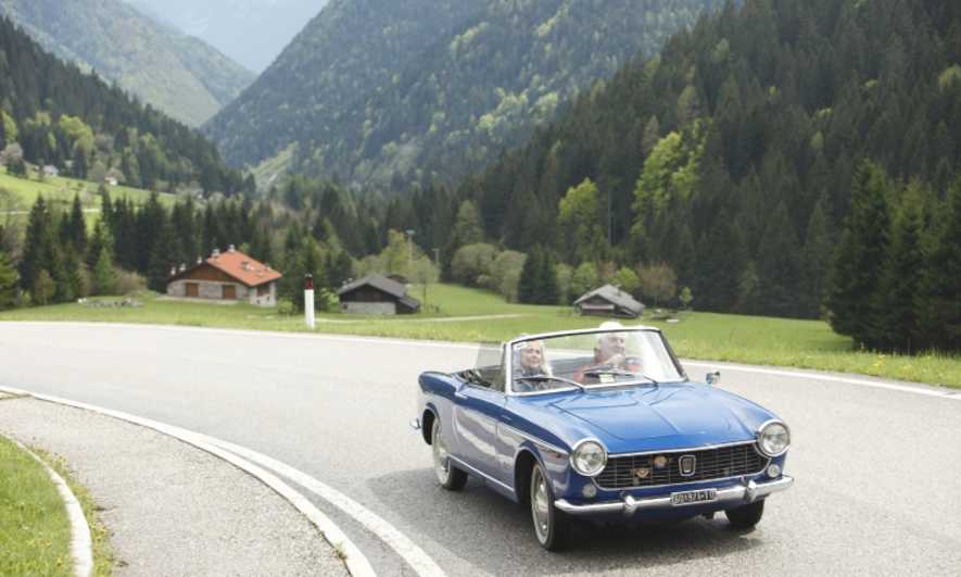 A retired couple drive a convertible through the mountains
