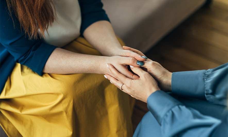 Two women seated on a couch, holding hands, illustrating the importance of companionship in mental health journeys.