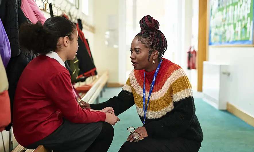A teacher kneels down to talk to a student