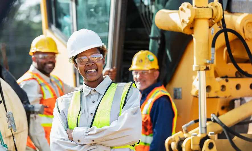 Construction worker with safety glasses, vest and hard hat on a construction site staring at the camera, smiling.