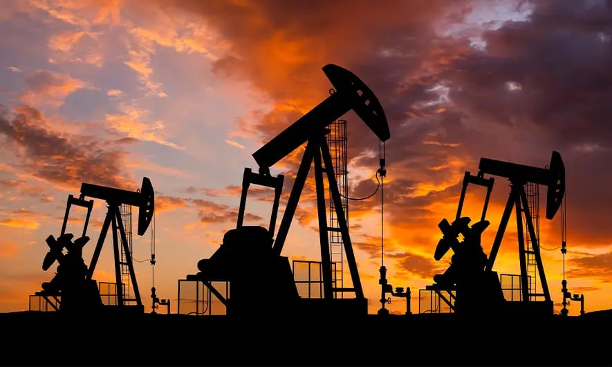 Energy worker with safety glasses, hat and safety vest using a laptop in front of an energy plant