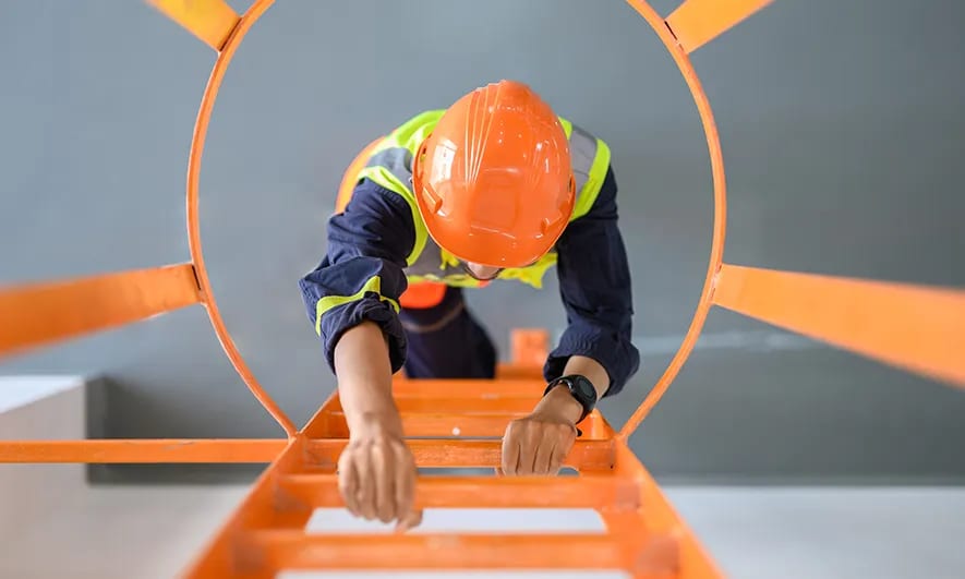 Worker in safety hat and vest climbing a steel ladder