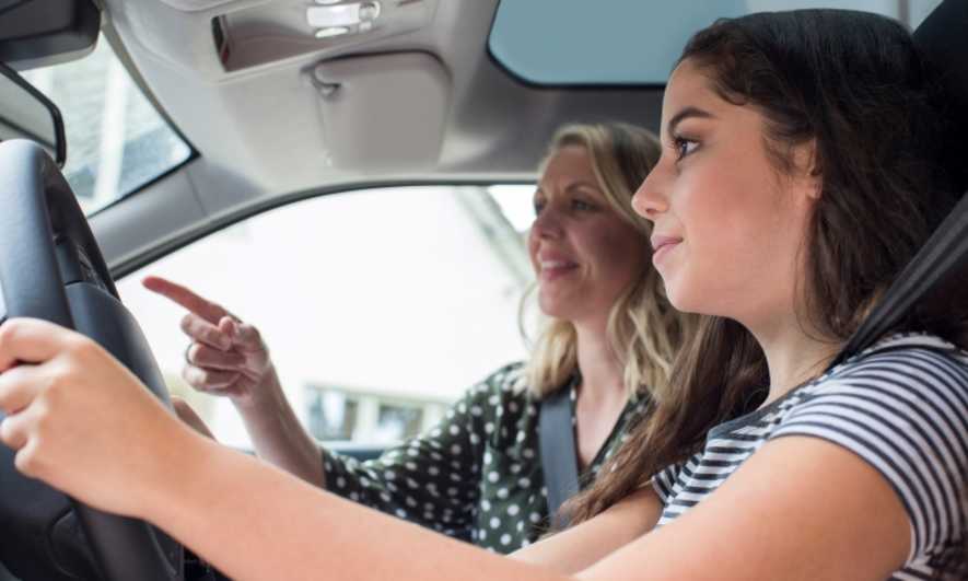 A teenager driving with their Mom in the passenger seat