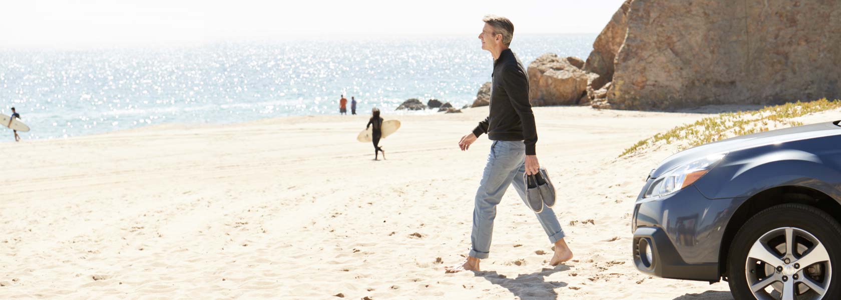 a man protected by types of car insurance walking on the beach in front of his car