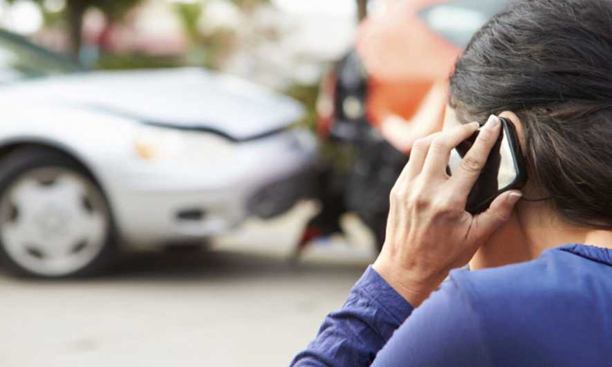 A person on the phone in front of a car crash