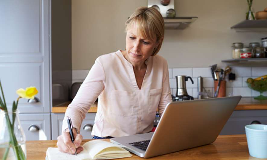 A woman sits at a laptop taking notes
