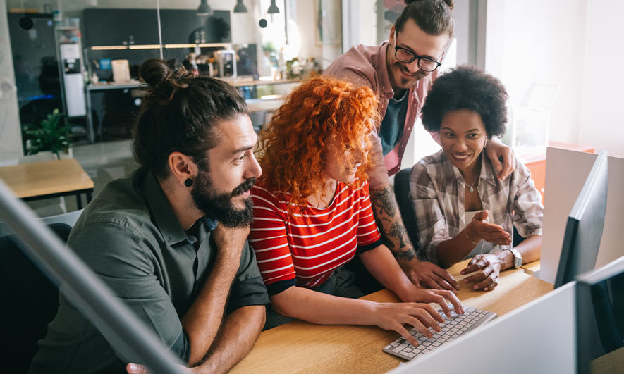 A diverse group of employees supporting each other around a laptop