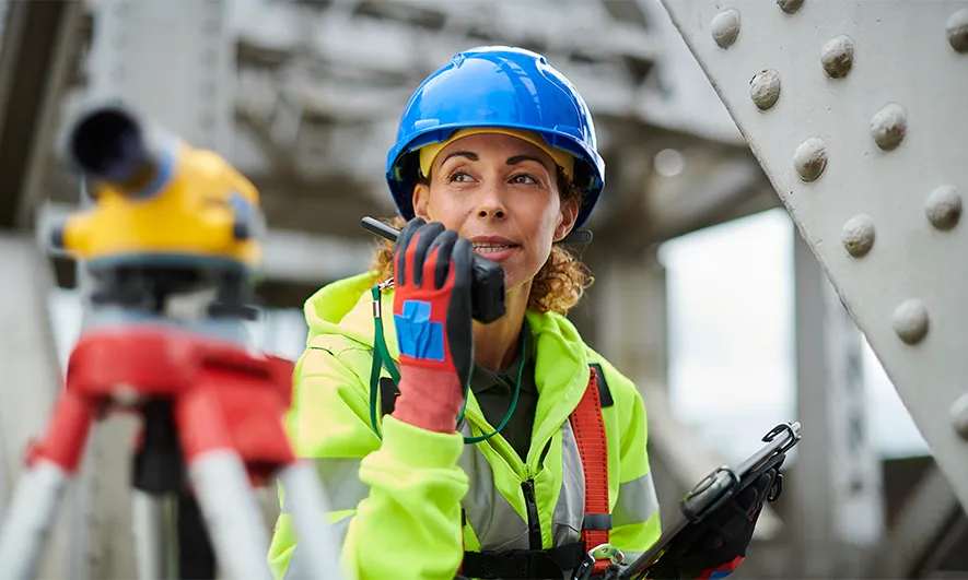 Woman on a jobsite speaks into a walkie-talkie