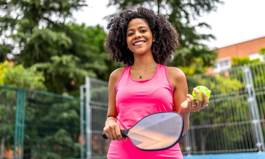 A woman laying tennis and smiling at the camera
