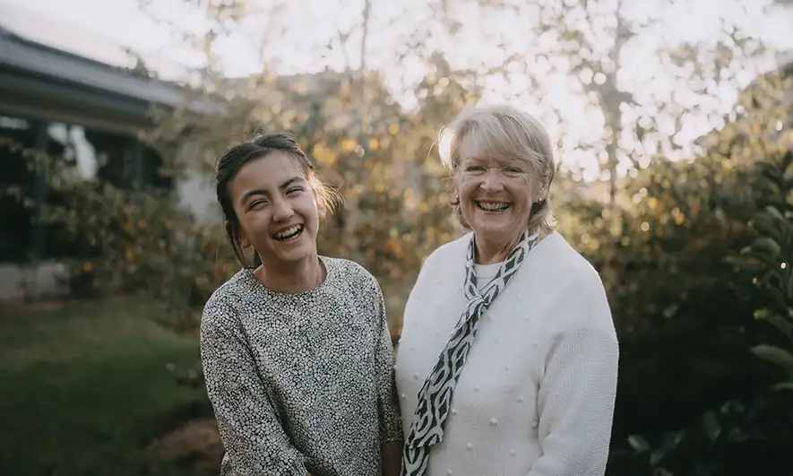 Grandma and granddaughter smile in a backyard
