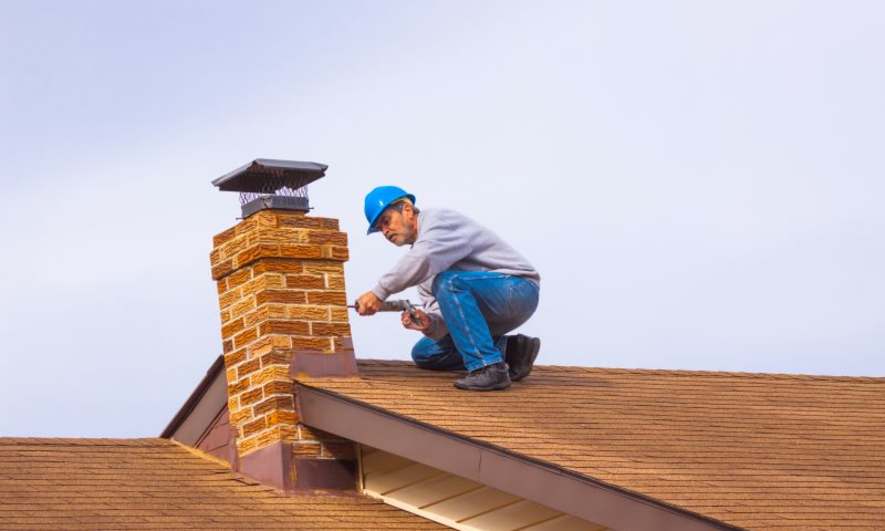 Man on a roof caulking a chimney