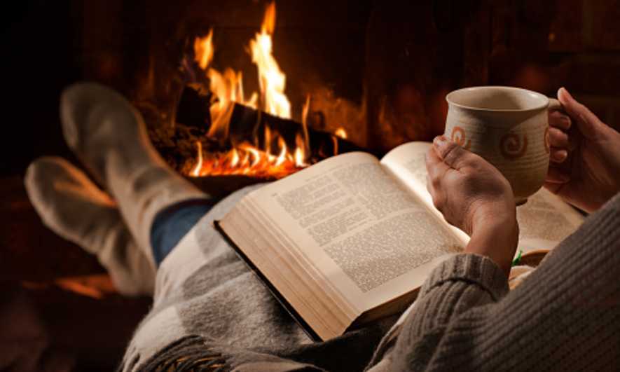 Person sitting in front of a fire reading a book