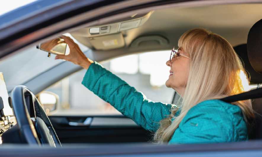 Mujer ajusta el espejo retrovisor en el carro